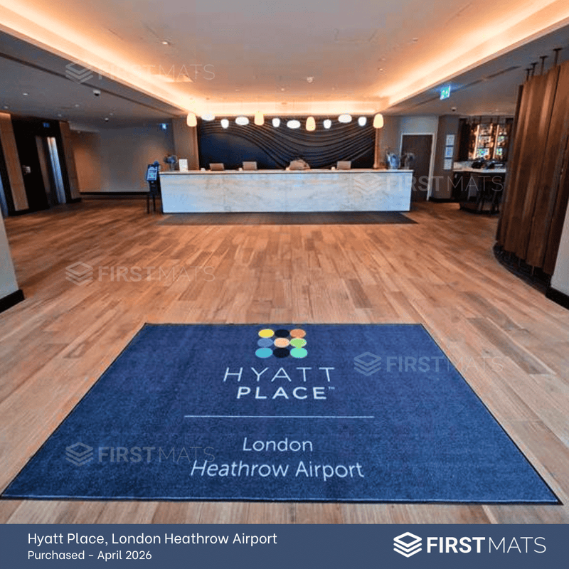Blue Hyatt Place logo mat in a lobby with wooden flooring and a reception desk.