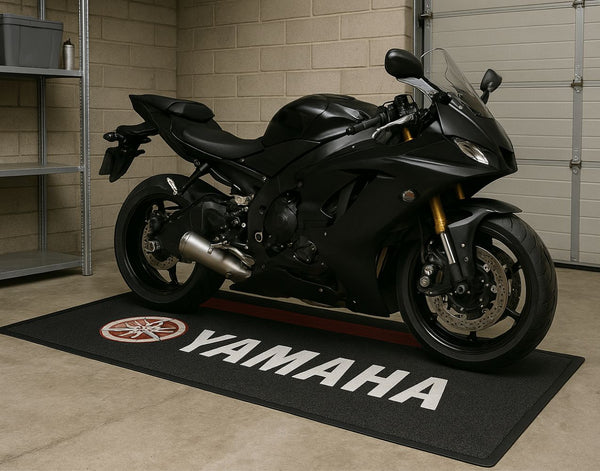 A black motorcycle parked on a black custom floor mat with the Yamaha logo displayed in the center of the mat.