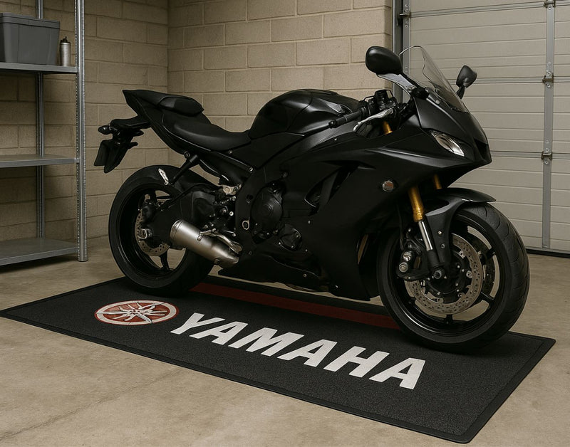 A black motorcycle parked on a black custom floor mat with the Yamaha logo displayed in the center of the mat.