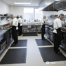 Chefs working in a professional kitchen with black scraper mats on the floor.