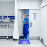 Nurse in blue scrubs standing in a medical setting with a blue mat on the floor.