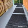 Black textured mats on a gray floor in a modern indoor setting with wooden walls and large windows.