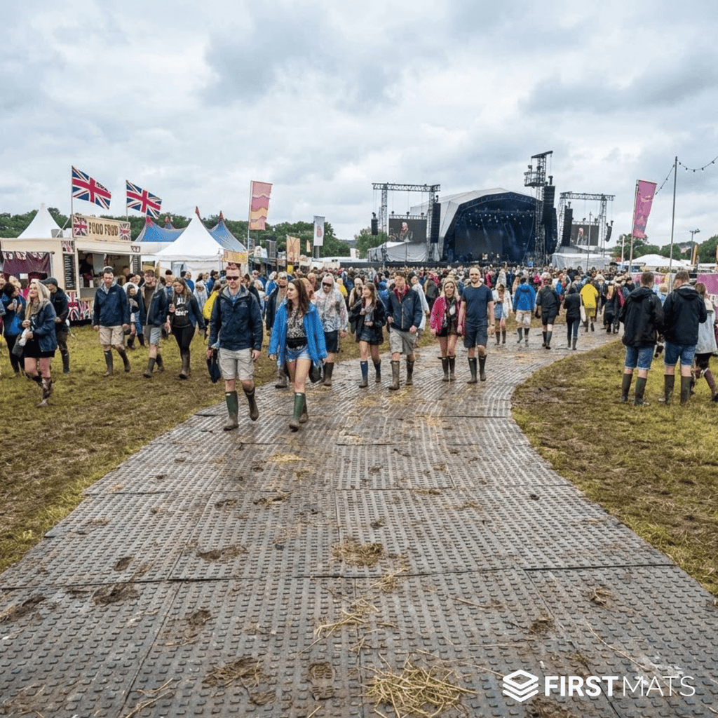 People walking on ground protection mats at a festival with tents and stage in the background