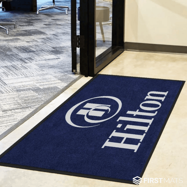 Navy blue doormat with Hilton logo on a floor transition between two carpeted areas.