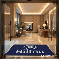 Hilton hotel entrance with glass doors and a blue doormat with Hilton logo.