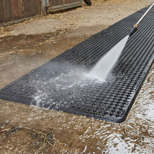 Black rubber mat being cleaned with a high-pressure water hose on a wet surface.