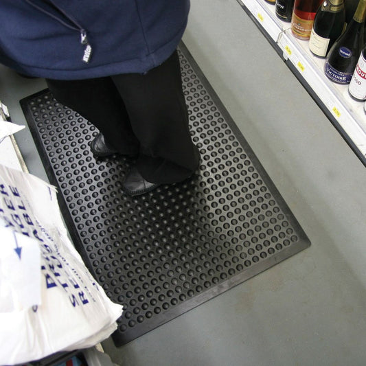 Person standing on a textured black mat in a store setting with shelves in the background.