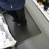 Person standing on a textured black mat in a store setting with shelves in the background.