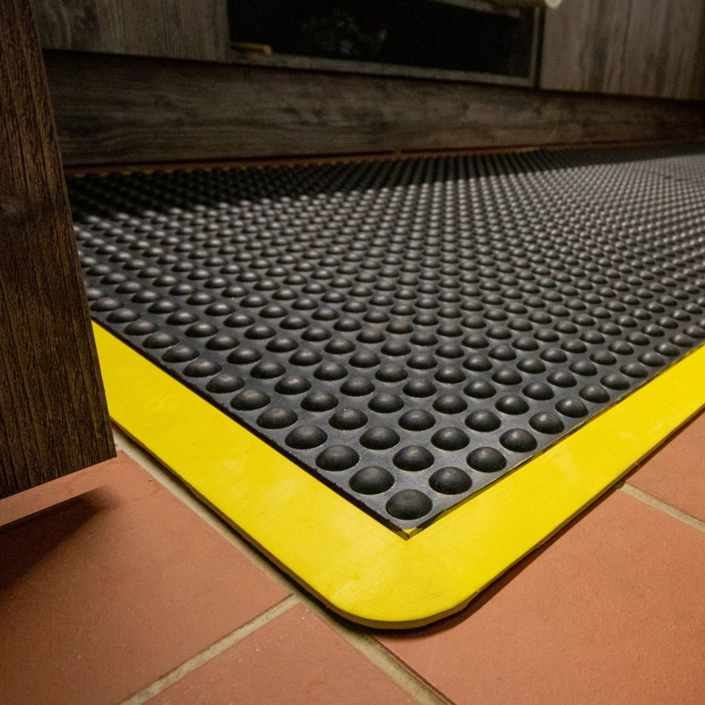 Black textured mat with yellow border on a tiled floor