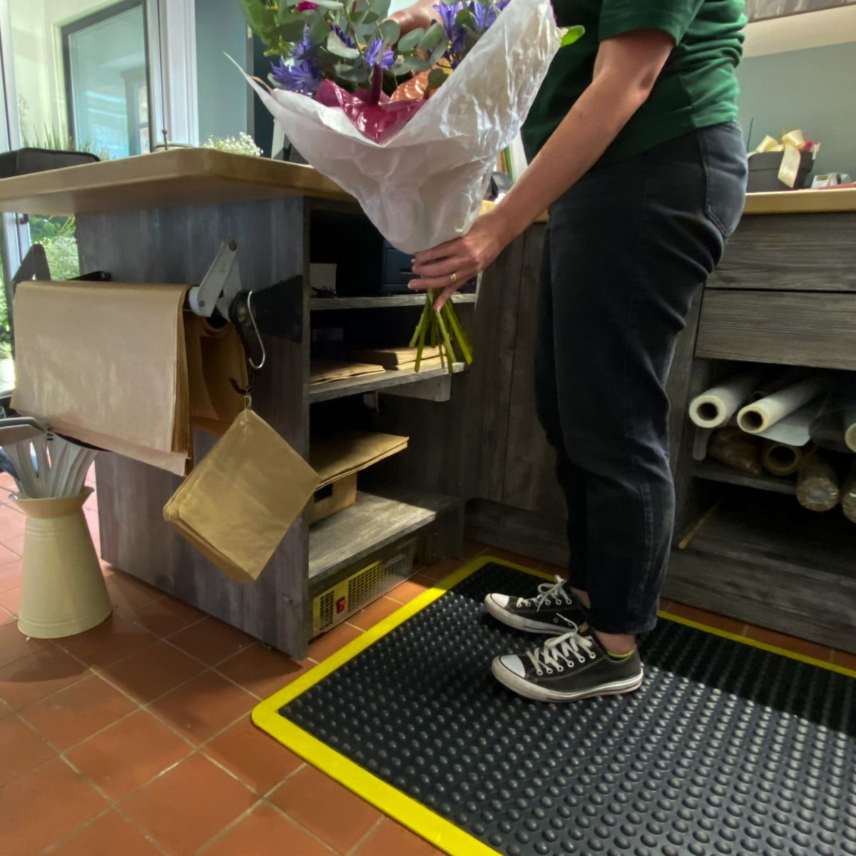 Person holding a bouquet of flowers in an indoor setting with shelves and tools.