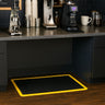 Black and yellow mat on a wooden floor in front of a kitchen counter with coffee-making equipment.