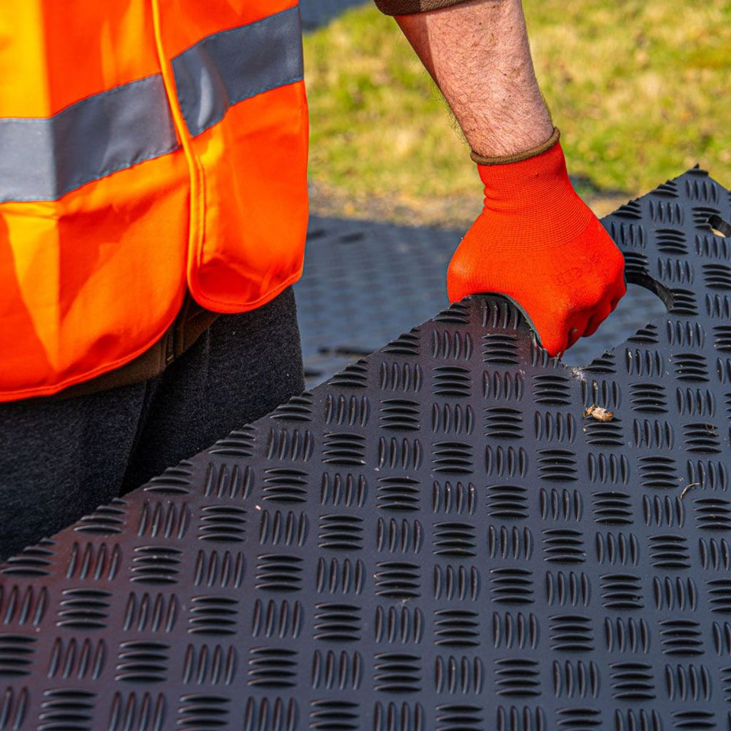 Person wearing an orange safety vest and gloves working on a heavy duty ground protect tile