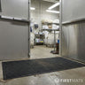Commercial kitchen with a metal door and black mat on the floor.
