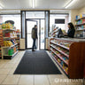Interior of a convenience store with a person entering through a glass door, and a heavy-duty entrance mat on the floor.