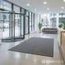 Modern hotel lobby with glass doors, grey floor mat, and reception desk.