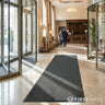 Modern hotel lobby with a grey doormat, glass doors, and reception desk.
