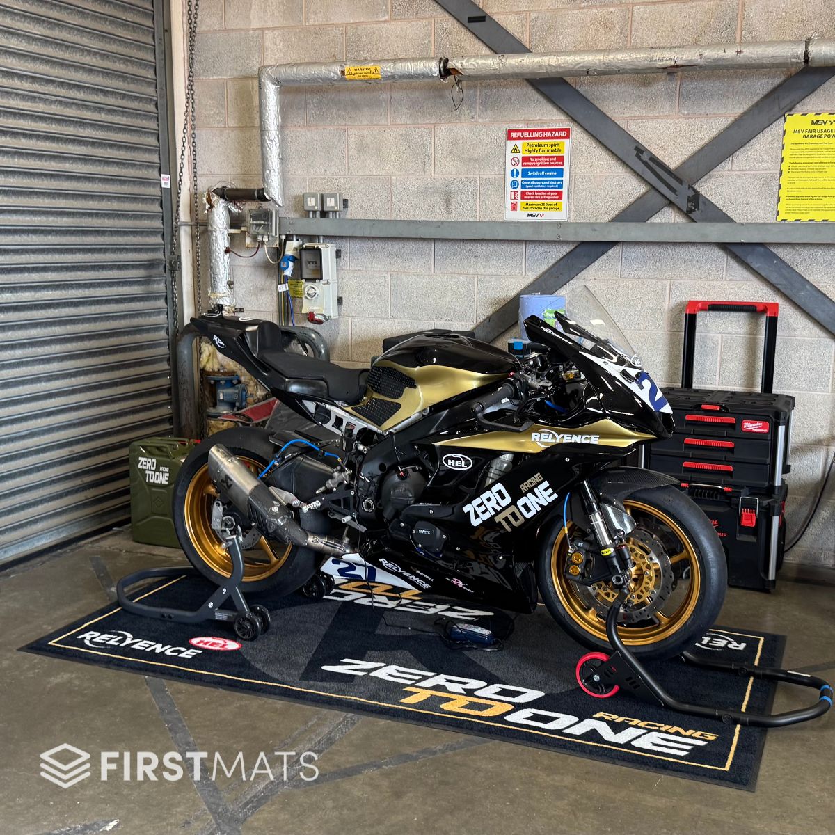 Motorcycle on a branded mat in a garage setting with tools and equipment around.