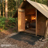 Wooden cabin in a forest with open door, and a rubber door mat at the entrance.