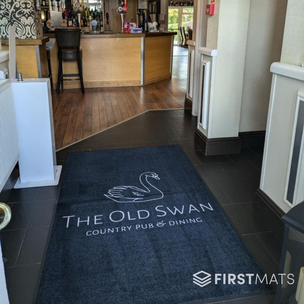 Blue rug with 'The Old Swan Country Pub & Dining' logo on a tiled floor, with a bar area in the background.
