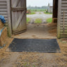 Black mat on a farmyard floor with hay and wooden structures in the background
