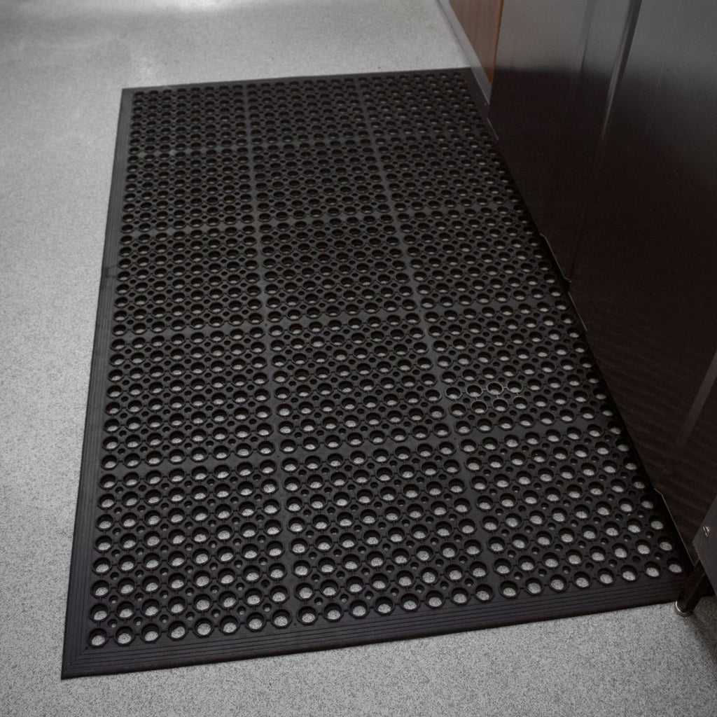 Black doormat with a textured pattern on a gray floor.