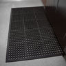 Black doormat with a textured pattern on a gray floor.