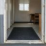Black mat on a portacabin floor with a door open to an indoor setting.