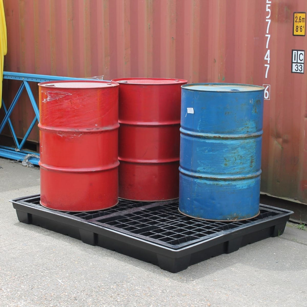 Red and blue barrels on a black plastic pallet in front of a red shipping container.