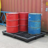 Red and blue barrels on a black plastic pallet in front of a red shipping container.