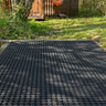 Black plastic grid on a grassy area with a wooden shed in the background