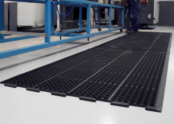 Interlocking black heavy-duty anti-fatigue mats designed for industrial workshop environments to provide comfort and reduce strain on feet and legs.
